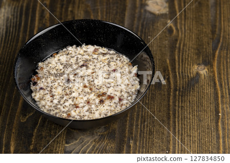 boiled oatmeal porridge with dried berries and fruits in a black bowl , cooking instant oatmeal porridge, chia in porridge, top view boiled oatmeal porridge with dried berries and fruits in a black bowl , cooking instant oatmeal porridge, chia in porridge, top view 127834850