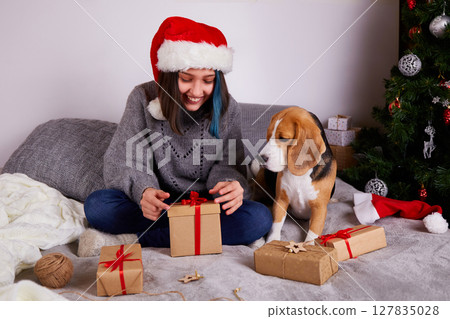 A girl in a Santa Claus hat opens a gift box. 127835028