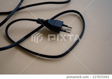 Electric European plug isolated on beige background. Black power cable with plug. Power cord close-up Electric European plug isolated on beige background. Black power cable with plug. Power cord close-up 127835042