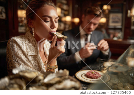 Elegant Indulgence Couple Enjoying Fine Dining with Fresh Oysters and Gourmet Dishes in a Luxurious Restaurant Setting 127835400