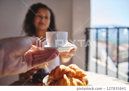 Warm summer morning featuring freshly brewed coffee, buttery croissants, and serene joy shared with a companion on a sunny balcony with a pleasant, scenic background. 127835841