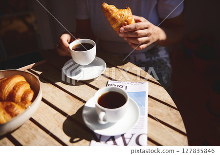 Table setting with coffee, croissants, and a magazine, portraying a peaceful morning routine in natural sunlight. 127835846