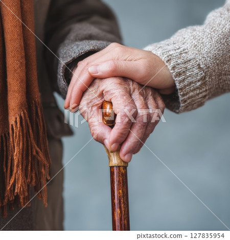 Compassionate Support: Gentle Hand Holding a Senior's Hand on a Cane, Symbolizing Care, Empathy, and Assistance in Elderly Well being Compassionate Support: Gentle Hand Holding a Senior's Hand on a Cane, Symbolizing Care, Empathy, and Assistance in Elderly Well being 127835954