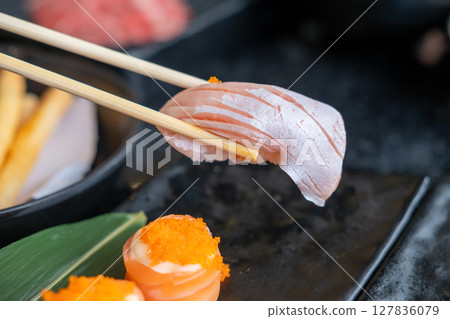 Chopsticks holding salmon sushi, in the restaurant Chopsticks holding salmon sushi, in the restaurant 127836079