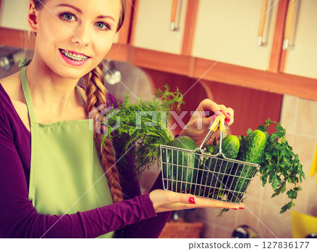 Woman in kitchen having vegetables holding shopping basket Woman in kitchen having vegetables holding shopping basket 127836177