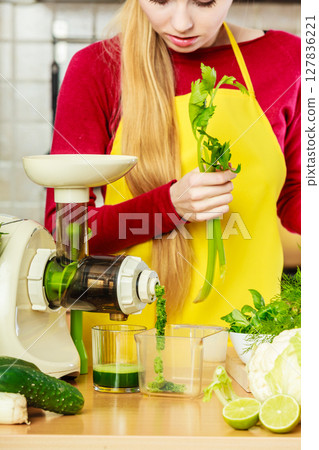 Woman in kitchen making vegetable smoothie juice 127836221