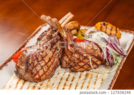 Grilled lamb chops served with flatbread, grilled vegetables, and fresh onion salad on a rustic ceramic platter 127836246