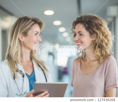 Empathetic doctor and smiling patient engage in a positive medical consultation, discussing health and well-being with a tablet in a modern clinic setting. 127836268