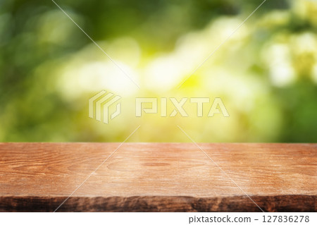 A smooth wooden tabletop set against a bright, sun-dappled green background, perfect for showcasing natural products or summer-themed content A smooth wooden tabletop set against a bright, sun-dappled green background, perfect for showcasing natural products or summer-themed content 127836278