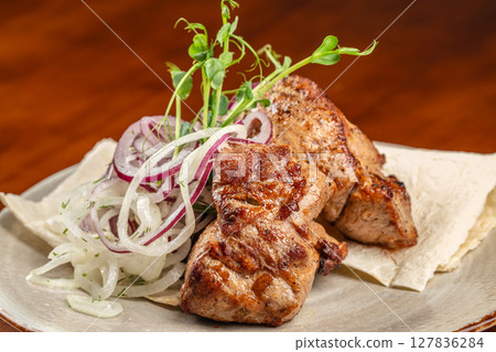 Juicy grilled pork served with fresh red and white onions on lavash bread, garnished with herbs, offering a savory and aromatic dining experience Juicy grilled pork served with fresh red and white onions on lavash bread, garnished with herbs, offering a savory and aromatic dining experience 127836284