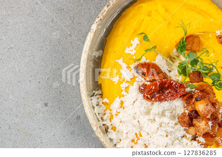 A vibrant bowl of creamy yellow polenta topped with grated cheese, roasted tomato, crispy pork bites, and fresh herbs offers a comforting and colorful meal 127836285