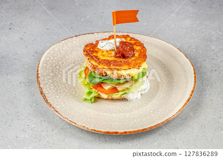 A gourmet burger stacked with crispy chicken, cheese, lettuce, tomato, onion, creamy sauce, and toasted patties, topped with a flag for a colorful presentation A gourmet burger stacked with crispy chicken, cheese, lettuce, tomato, onion, creamy sauce, and toasted patties, topped with a flag for a colorful presentation 127836289