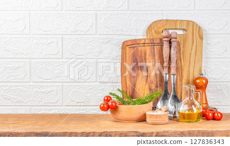 A warm rustic kitchen arrangement featuring wooden cutting boards, utensils, fresh cherry tomatoes, rosemary, olive oil, and salt on a wooden countertop against a white brick wall A warm rustic kitchen arrangement featuring wooden cutting boards, utensils, fresh cherry tomatoes, rosemary, olive oil, and salt on a wooden countertop against a white brick wall 127836343