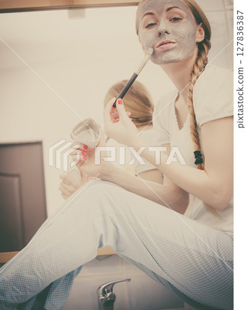 Woman applying with brush clay mud mask to her face 127836387