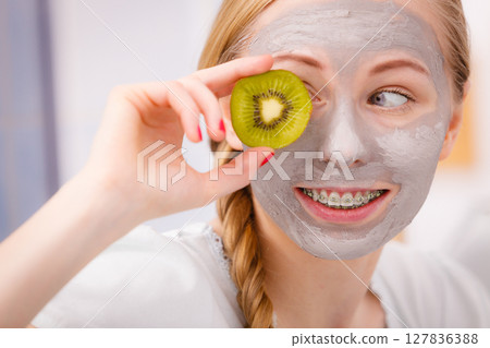 Happy young woman having face mask holding kiwi Happy young woman having face mask holding kiwi 127836388