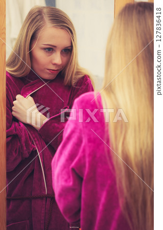 Woman looking at her reflection in mirror 127836418