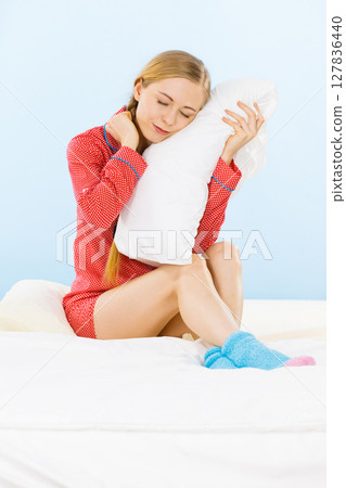 Young woman wearing pajamas hugging soft pillow 127836440