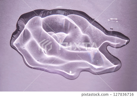 A drop of gel serum on a purple background with beautiful highlights. A drop of gel serum on a purple background with beautiful highlights. 127836716