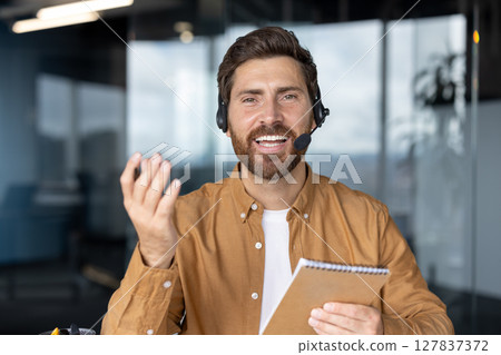 Business professional in virtual video call demonstrating communication skills. Engaging expression, wearing headset, holding notebook. Ideal for concepts of remote work, virtual meetings, technology 127837372