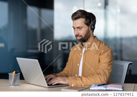 Mature businessman wearing headset engaged in video conference at office. Confident professional using laptop for online communication, showcasing skills in remote work and digital collaboration. Mature businessman wearing headset engaged in video conference at office. Confident professional using laptop for online communication, showcasing skills in remote work and digital collaboration. 127837451