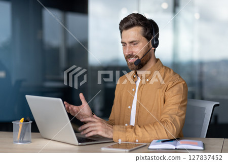 Mature businessman engaged in virtual meeting, wearing headset with laptop in office. Displays professional communication, remote work, technology use, modern business approach. Mature businessman engaged in virtual meeting, wearing headset with laptop in office. Displays professional communication, remote work, technology use, modern business approach. 127837452