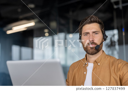 Mature businessman wearing headset engaging in video conference call while working in modern office. Confident expression reflects professional demeanor. Interaction emphasizes remote work setup. 127837499