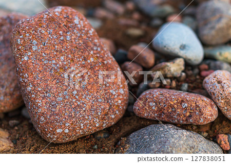 Large red stone with white grains interspersed close-up, lying on multi-colored stones. Natural ceramic materials in their natural environment, study of composition and origin Large red stone with white grains interspersed close-up, lying on multi-colored stones. Natural ceramic materials in their natural environment, study of composition and origin 127838051