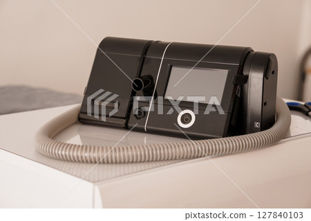 Modern Black CPAP Machine with Humidifier on White Table, Healthcare Technology Device, Sleep Apnea Treatment, Medical Equipment Close-Up 127840103