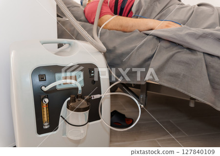 Patient Receiving Oxygen Therapy with Concentrator Machine in Modern Hospital Bed. White and Red Equipment, Clinical Setting, Healthcare Concept 127840109