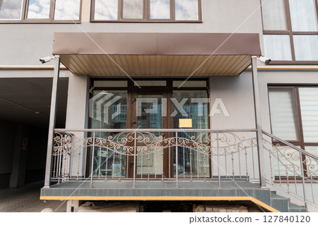 Elegant Building Entrance with Wrought Iron Balcony and Security Cameras, Modern Architecture, Neutral Palette, Exterior View, Commercial Real Estate. Elegant Building Entrance with Wrought Iron Balcony and Security Cameras, Modern Architecture, Neutral Palette, Exterior View, Commercial Real Estate. 127840120