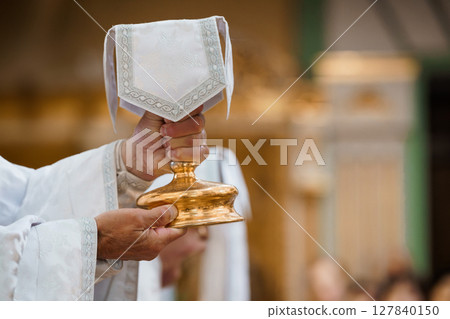 Catholic Priest Holding the Holy Eucharist Chalice During Religious Ceremony in Church Gold Interior 127840150