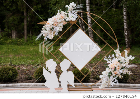 Romantic Outdoor Wedding Arch Ceremony with Floral Decor, Golden Frame, Couple Silhouettes, Lush Green Forest Backdrop, Peach and White Tones, Stylish Event 127840154