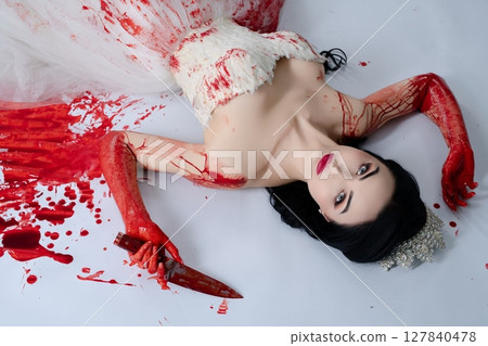 Bride in blood-soaked lingerie holds knife while lying on the floor 127840478