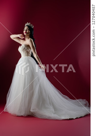 Elegant bride in stunning white gown poses like a princess against pink backdrop 127840487