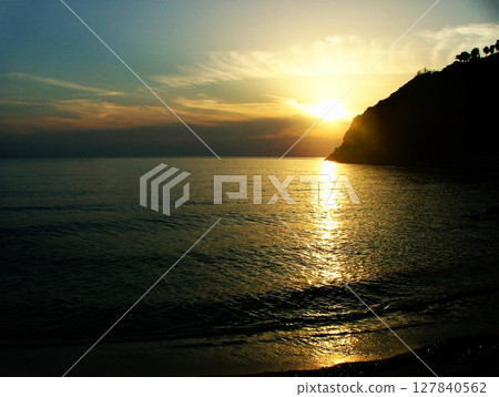 Breathtaking sunset over the Calabrian sea, with vibrant hues of orange, gold illuminating the sky. The calm water reflects the warm colors, while the rugged cliffs of Calabria. 127840562
