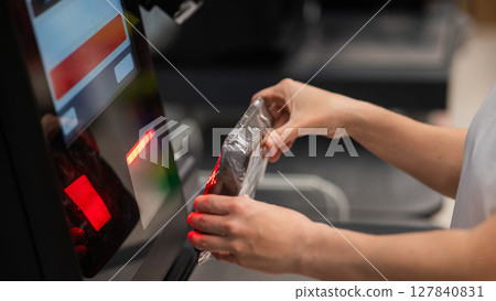Woman scanning a package of cucumbers at a self-service checkout.  127840831