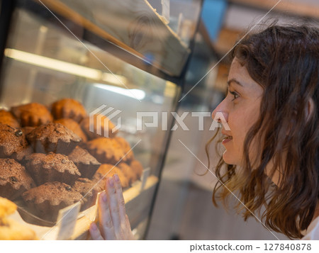 Caucasian woman looks greedily at baked goods in a bakery.  127840878