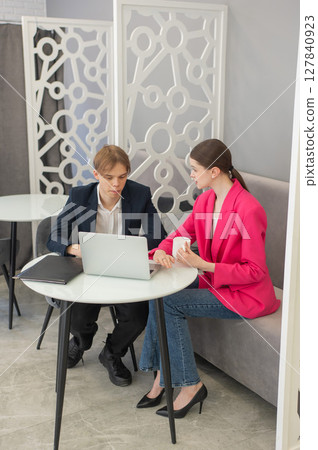 Colleagues are sitting at a laptop and discussing work.  127840923
