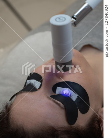 A woman undergoing eyelash extension procedure using an ultraviolet lamp. 127840924