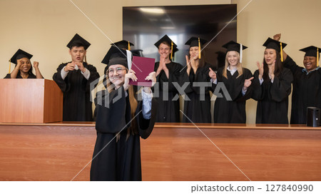 Happy Caucasian woman holds red diploma and classmates support her. Happy Caucasian woman holds red diploma and classmates support her. 127840990