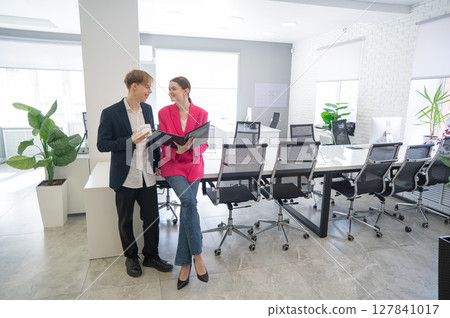 Colleagues look at a folder with documents and discuss work issues.  127841017