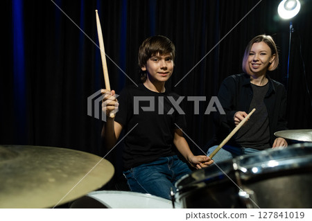 Young caucasian woman teaches a boy to play the drums in the studio on a black background. Music school student 127841019