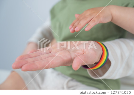 Caucasian woman with rainbow bracelet holds her one-year-old son's hand.  127841030