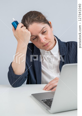Tired businesswoman smoking an electronic cigarette while working on a laptop. Tobacco heating system. 127841040