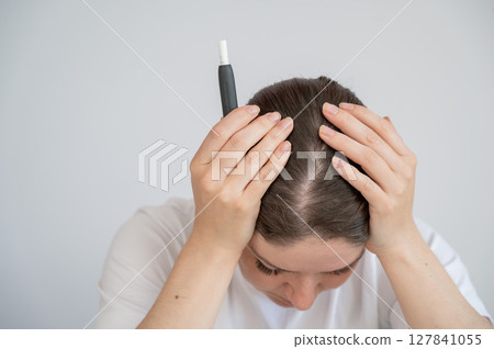 Tired woman smoking an electronic cigarette while working on a laptop. Tobacco heating system. 127841055