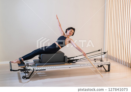 Asian woman doing pilates on reformer.  127841073