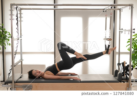 Asian woman doing pilates on reformer. Asian woman doing pilates on reformer. 127841080