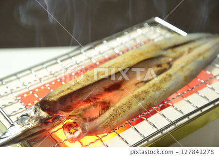Grilling filleted pacific saury on a charcoal grill with rising smoke 127841278