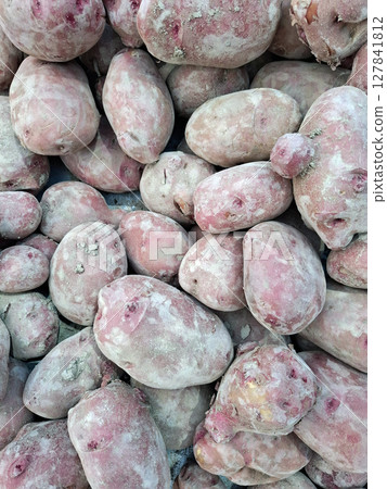 A variety of fresh red potatoes are piled together at a farmers market in Spain. Vendors and shoppers interact nearby, capturing the lively atmosphere of the market in the afternoon. 127841812