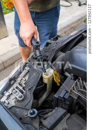 Man filling water into windscreen water tank in car engine room, for window wiper  127842117